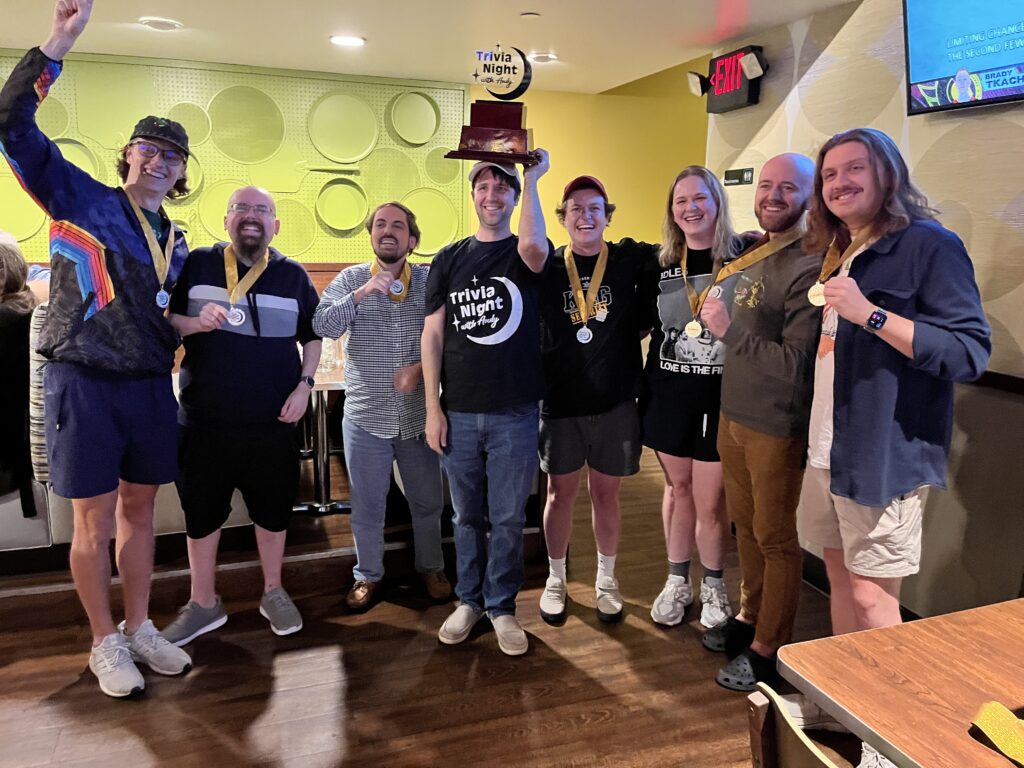 A group of people wearing medals in a bar. They won pub trivia championship.